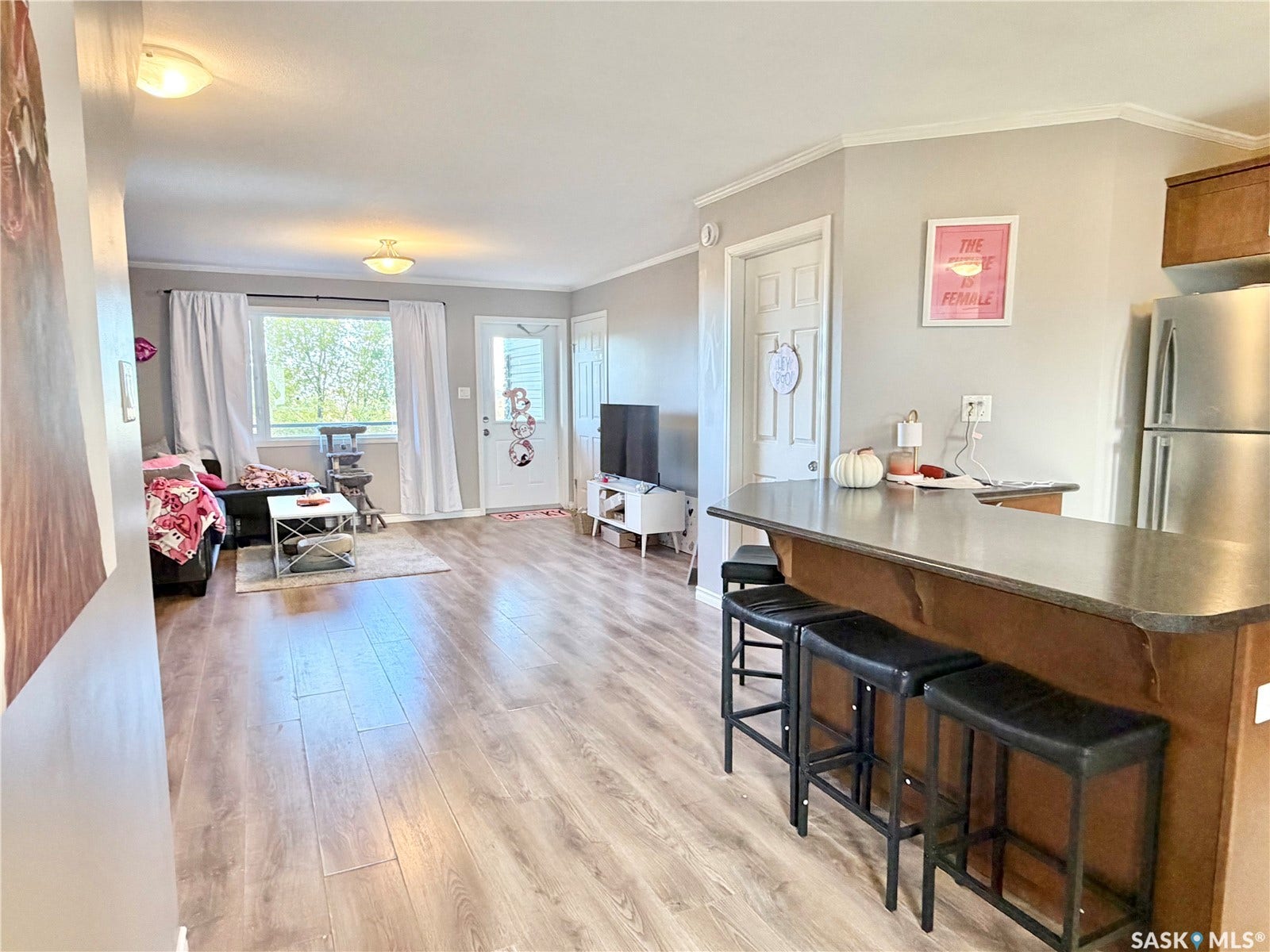 Open-concept living space featuring wood-finish flooring, a kitchen island with seating, and stainless steel refrigerator