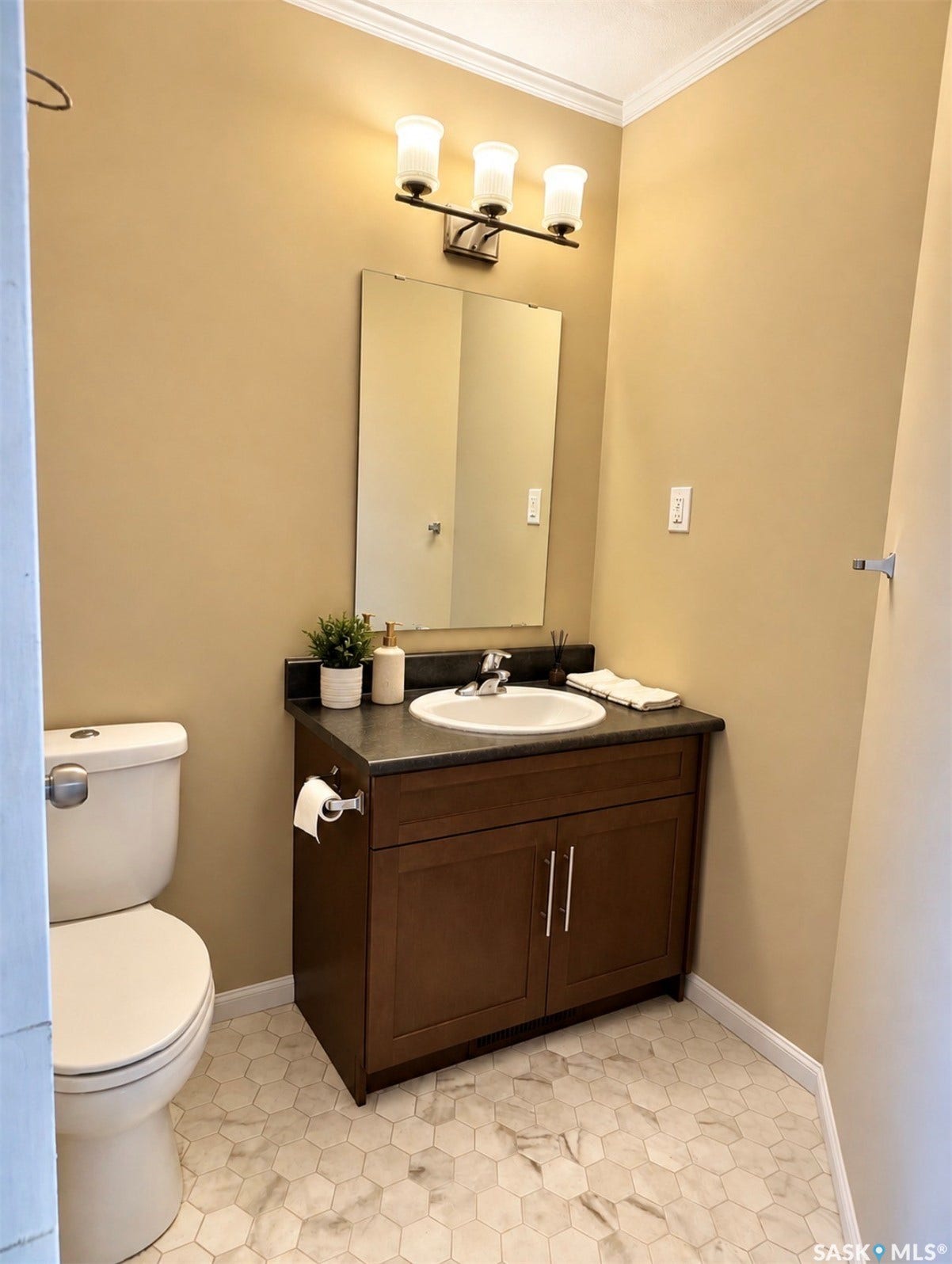 White hexagonal floor tiles, dark wood-finish vanity with a built-in sink, dark countertop, rectangular mirror, and a three-light fixture