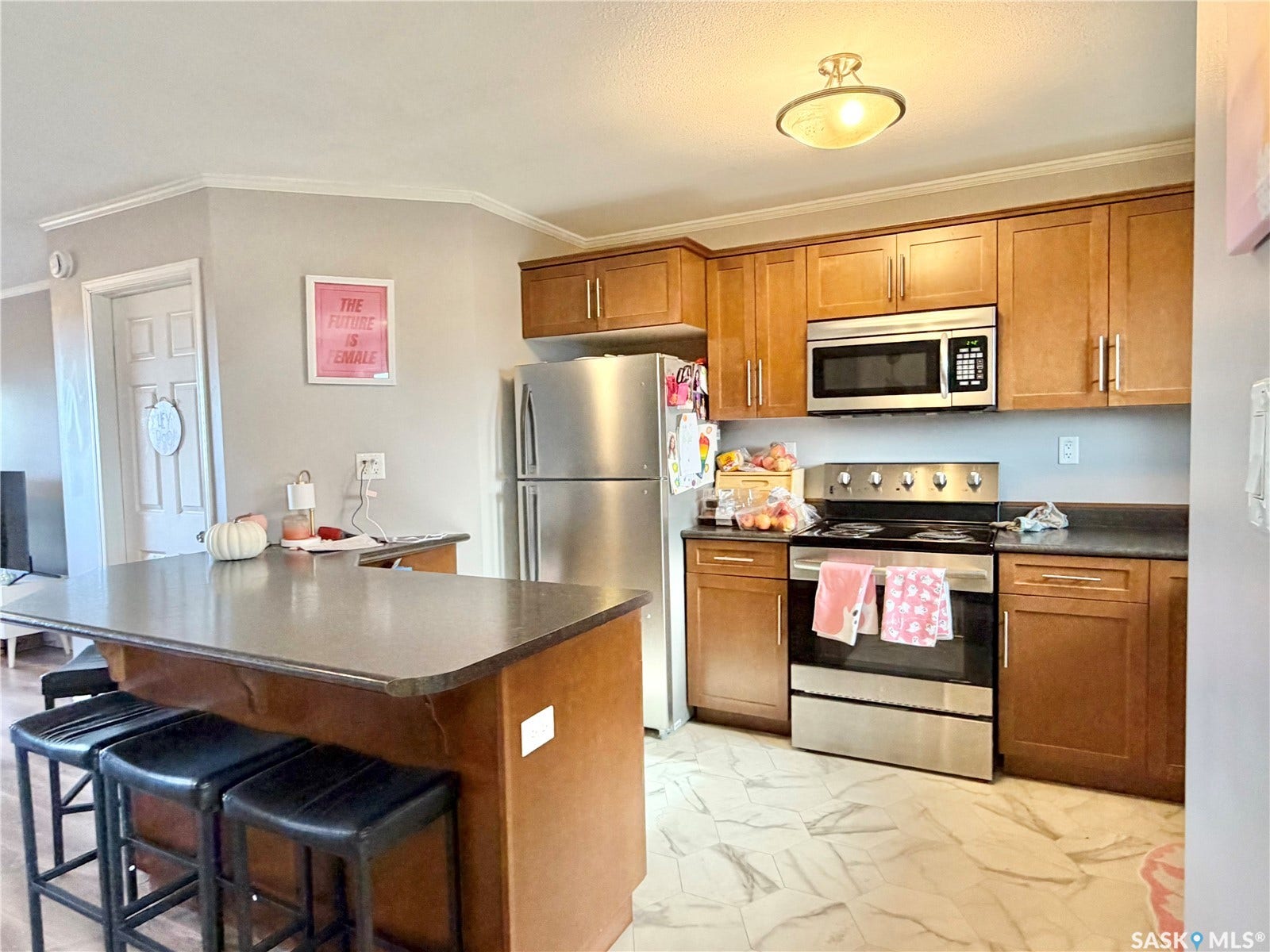 Kitchen featuring wood-finish cabinetry, stainless steel appliances, a center island with countertop seating, and crown molding