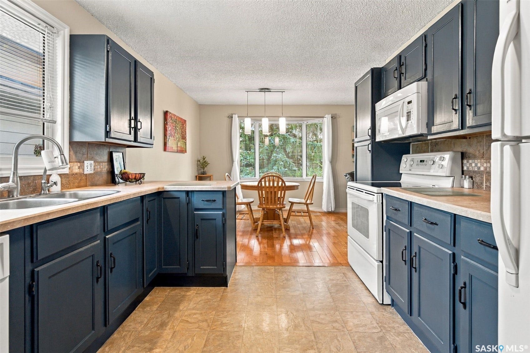 Kitchen featuring blue cabinetry, light countertops, integrated dual basin sink, and white appliances