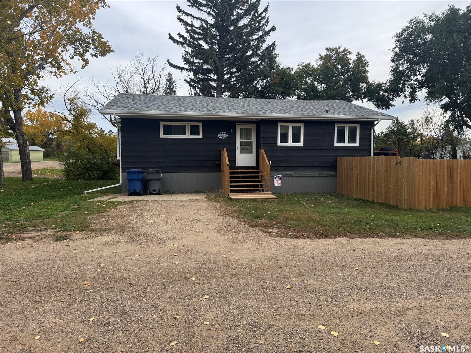 Dark-toned exterior siding with white window trim, wood entry steps, and a privacy fence
