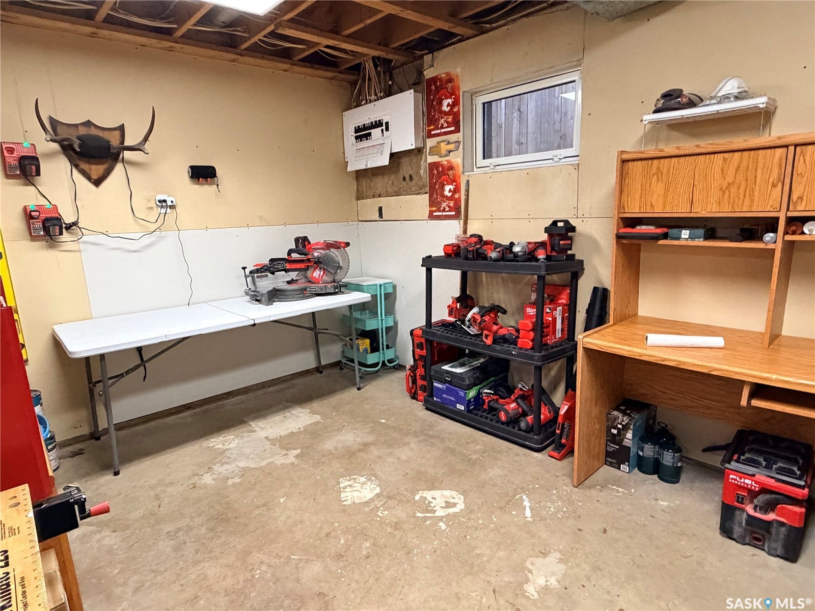 Unfinished concrete flooring, built-in wooden desk, and exposed ceiling joists