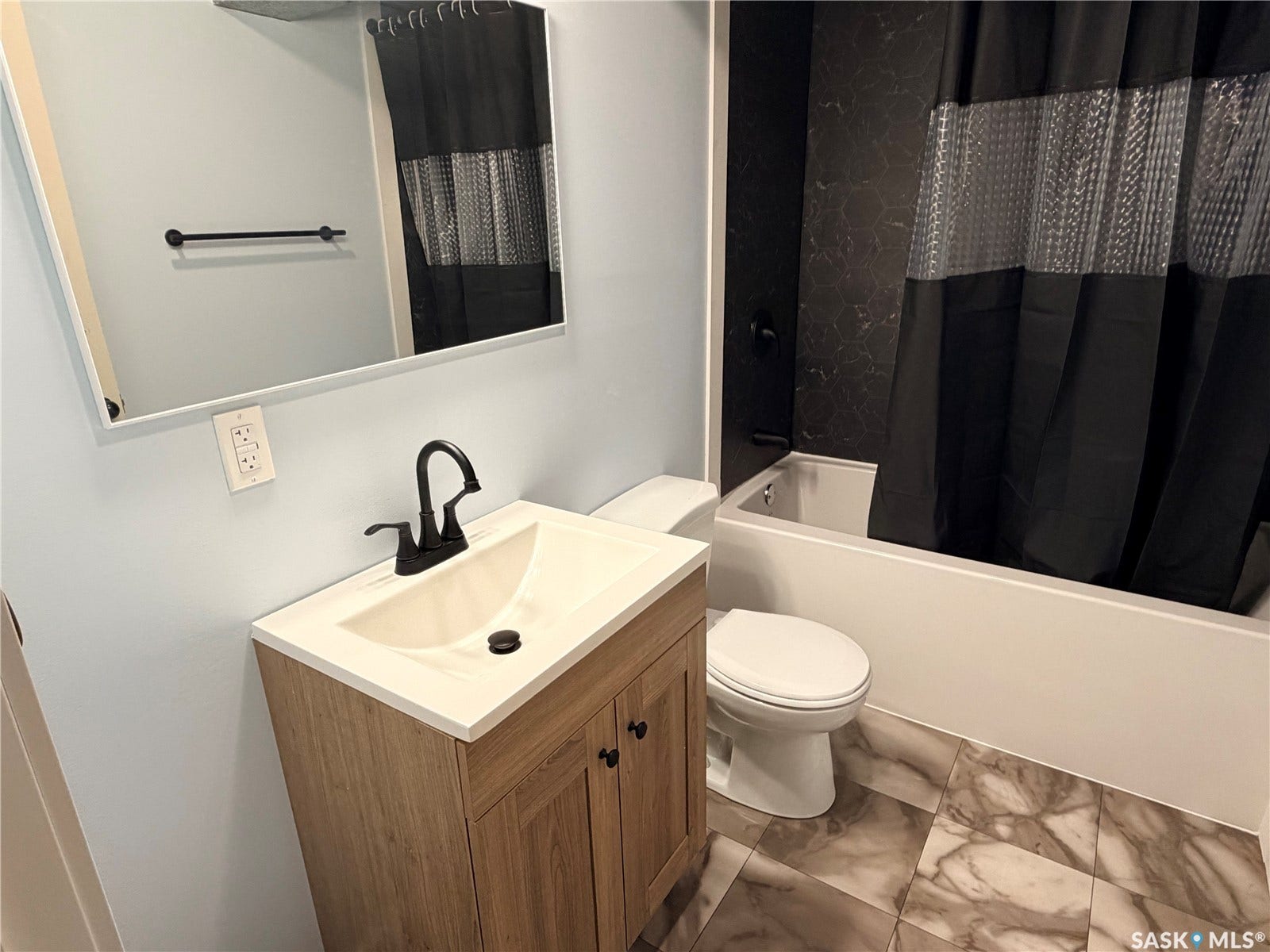 Bathroom featuring a wood-finish vanity with an integrated sink, matte black faucet, and a framed mirror