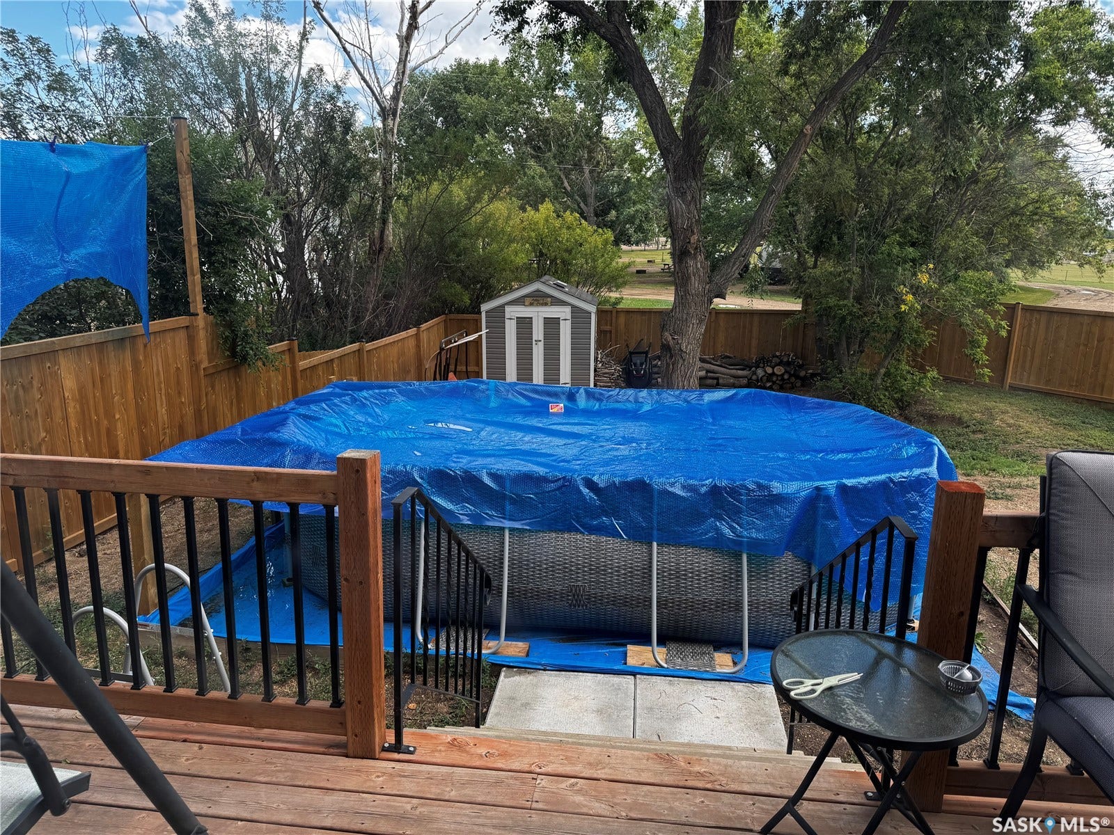 Expansive deck with wood flooring and dark railings, featuring an above-ground pool, a storage shed, and a privacy fence