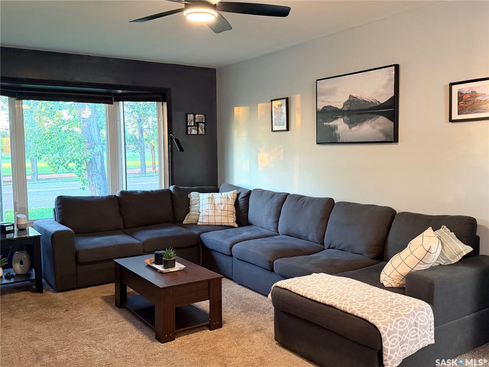 Bay window with multiple panes, ceiling fan with integrated lighting, and carpeted flooring