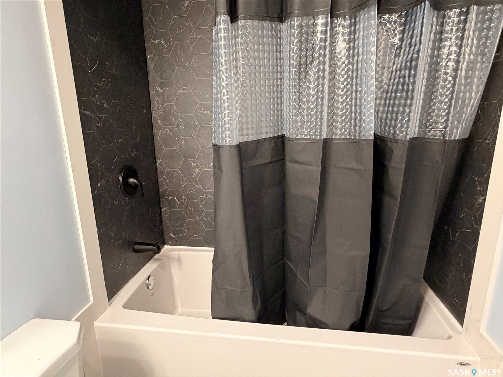 Bathtub with matte black fixtures and a tiled surround featuring a hexagonal pattern
