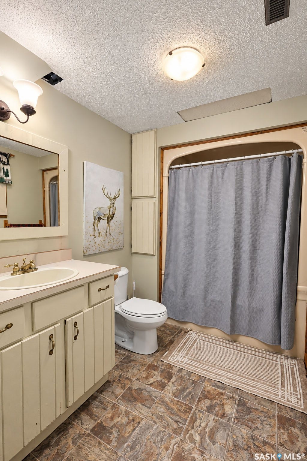 Vanity with integrated sink, patterned floor tiles, built-in storage cabinets, and a shower/tub combination