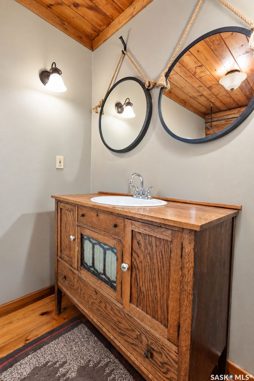 Wood-finish ceiling and flooring, wood vanity with integrated sink, two wall-mounted mirrors, and wall sconce lighting