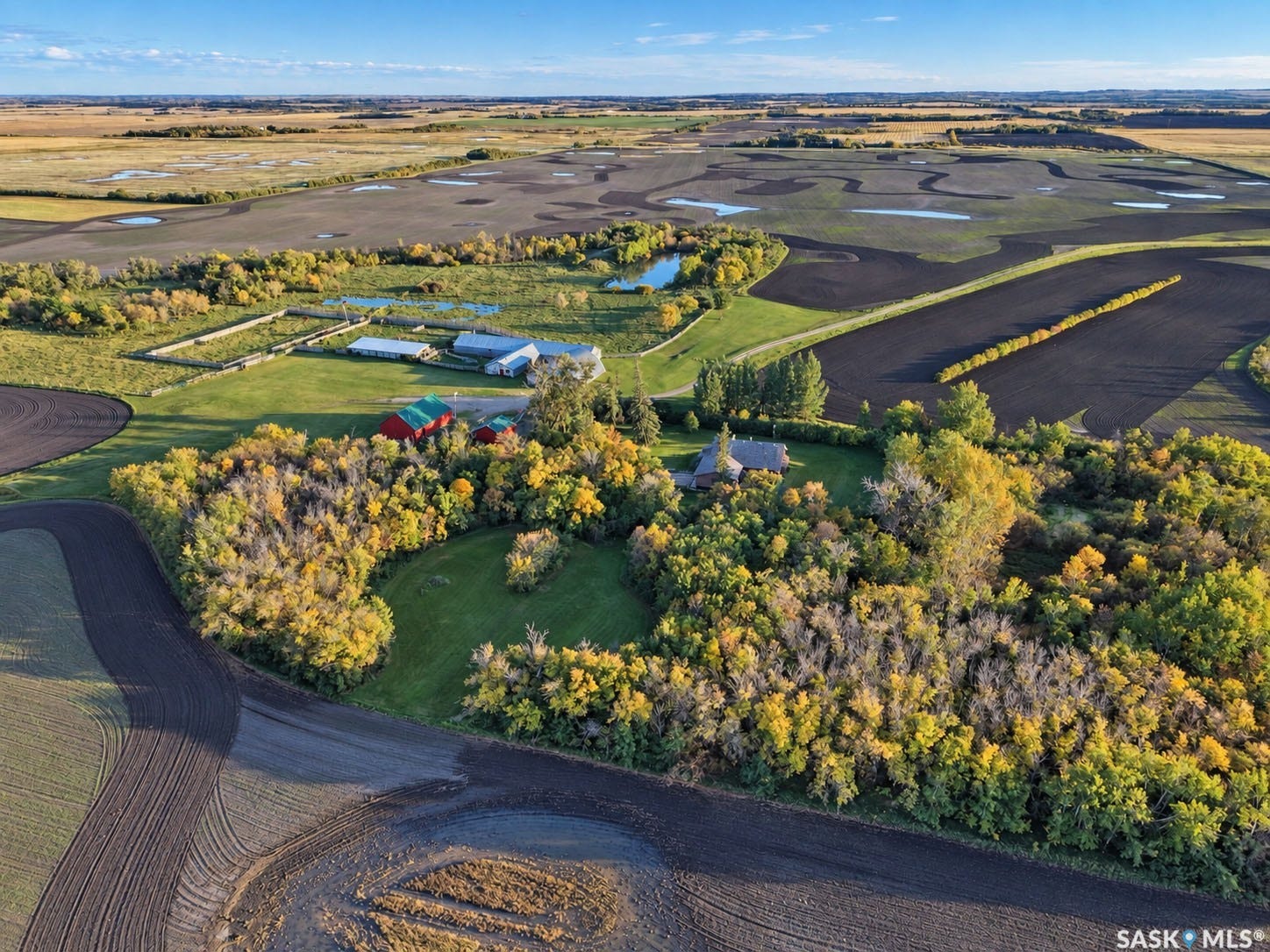Expansive rural landscape featuring a dwelling, agricultural fields, multiple outbuildings, and natural water features