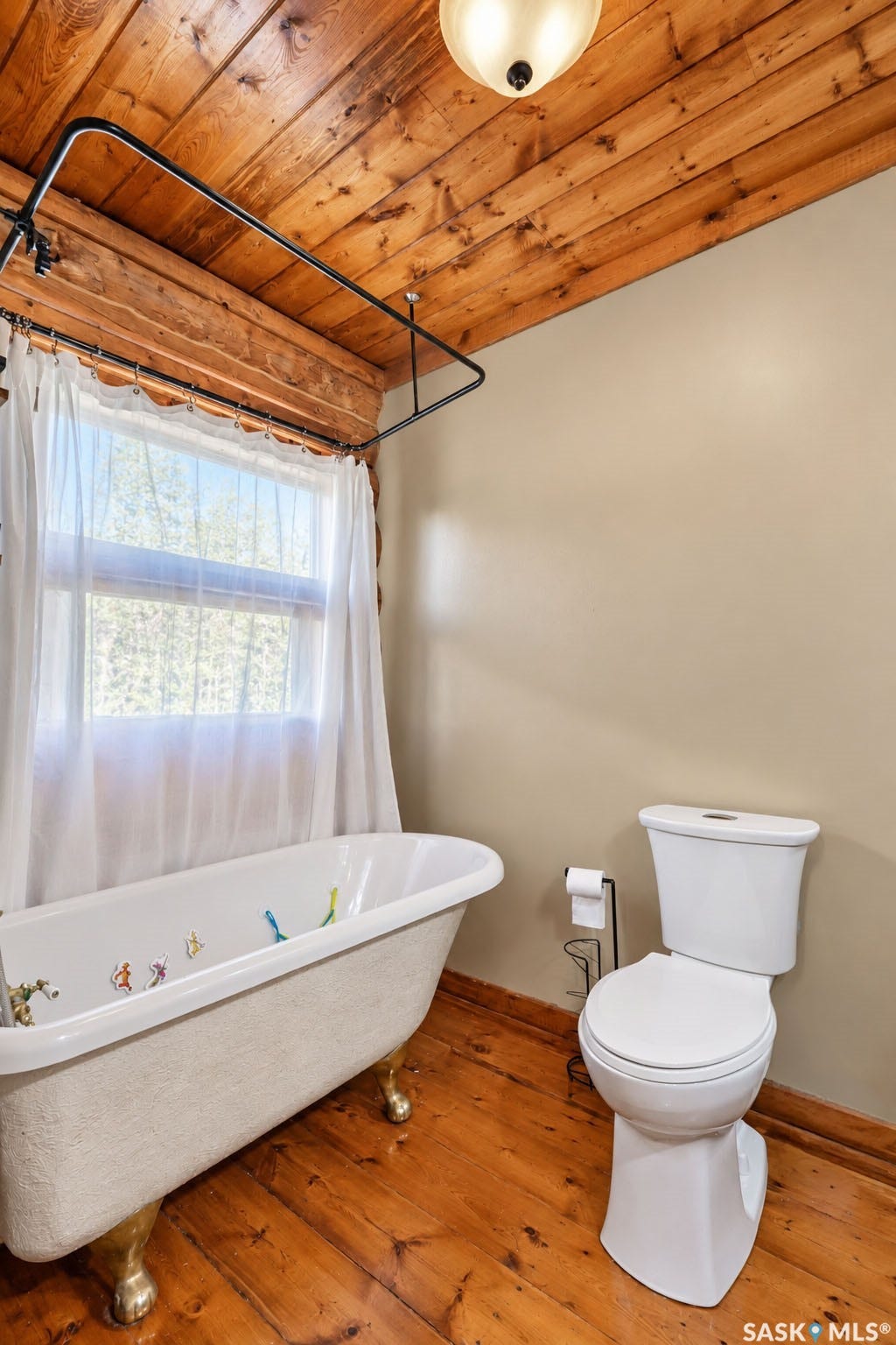 Wood-finish flooring, wood plank ceiling, clawfoot tub, white toilet, and window with natural light