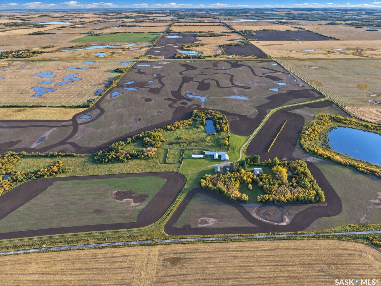 Expansive rural property featuring multiple cultivated fields, scattered natural water features, and an established building site with several structures
