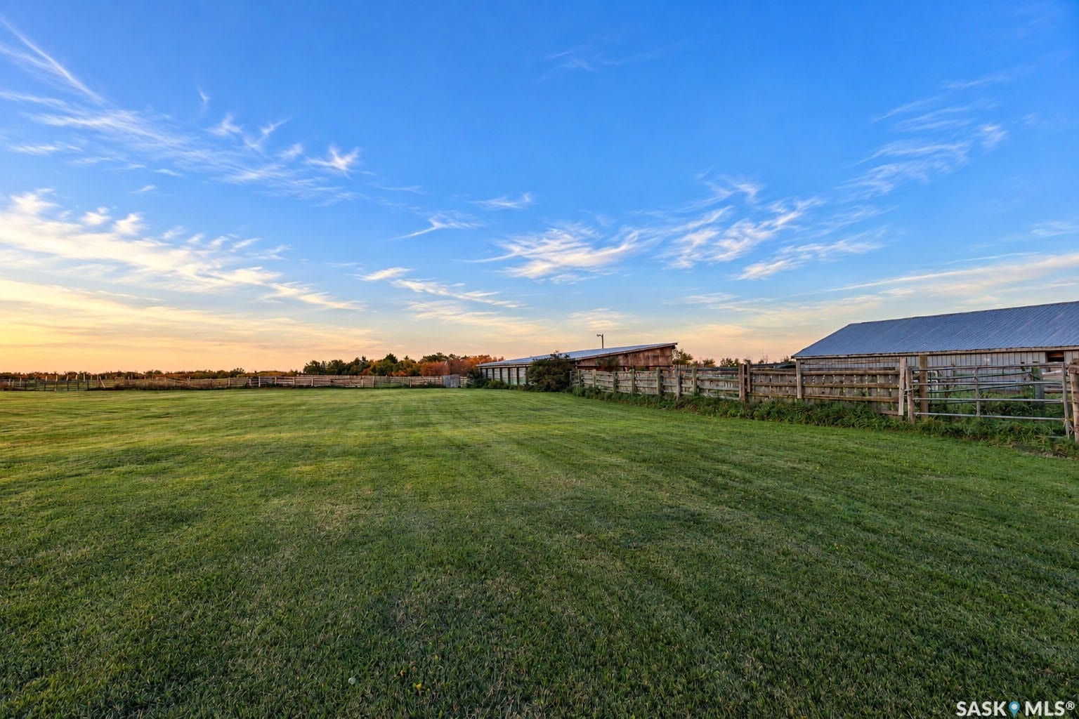 Expansive grassy field with perimeter fencing, accompanied by two agricultural structures with metal roofs