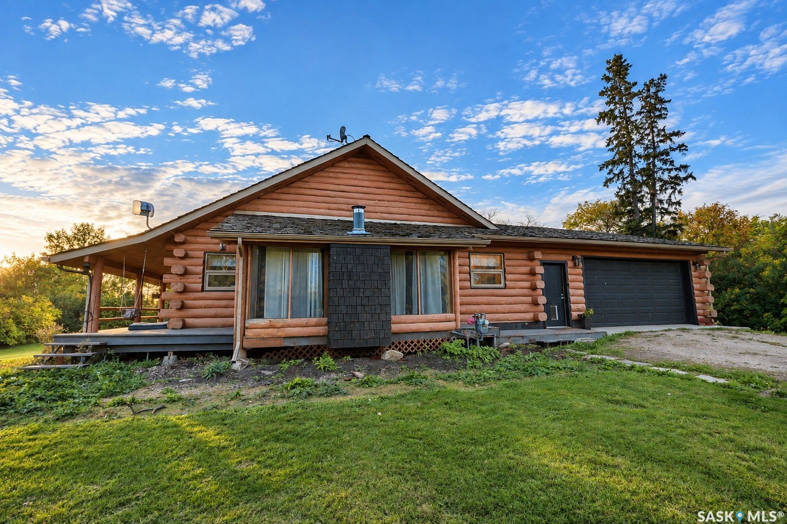 Log cabin exterior with a covered porch, attached two-car garage, and a sloped front lawn