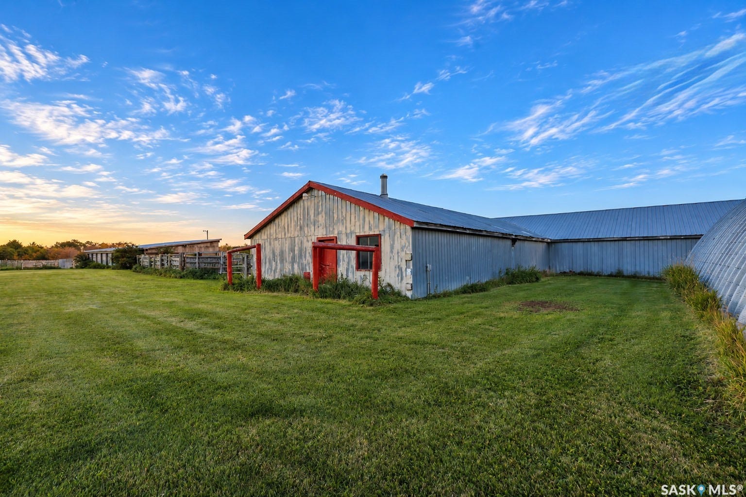 Expansive grassy area with multiple utility structures featuring metal siding, a red trim barn, and a metal roof