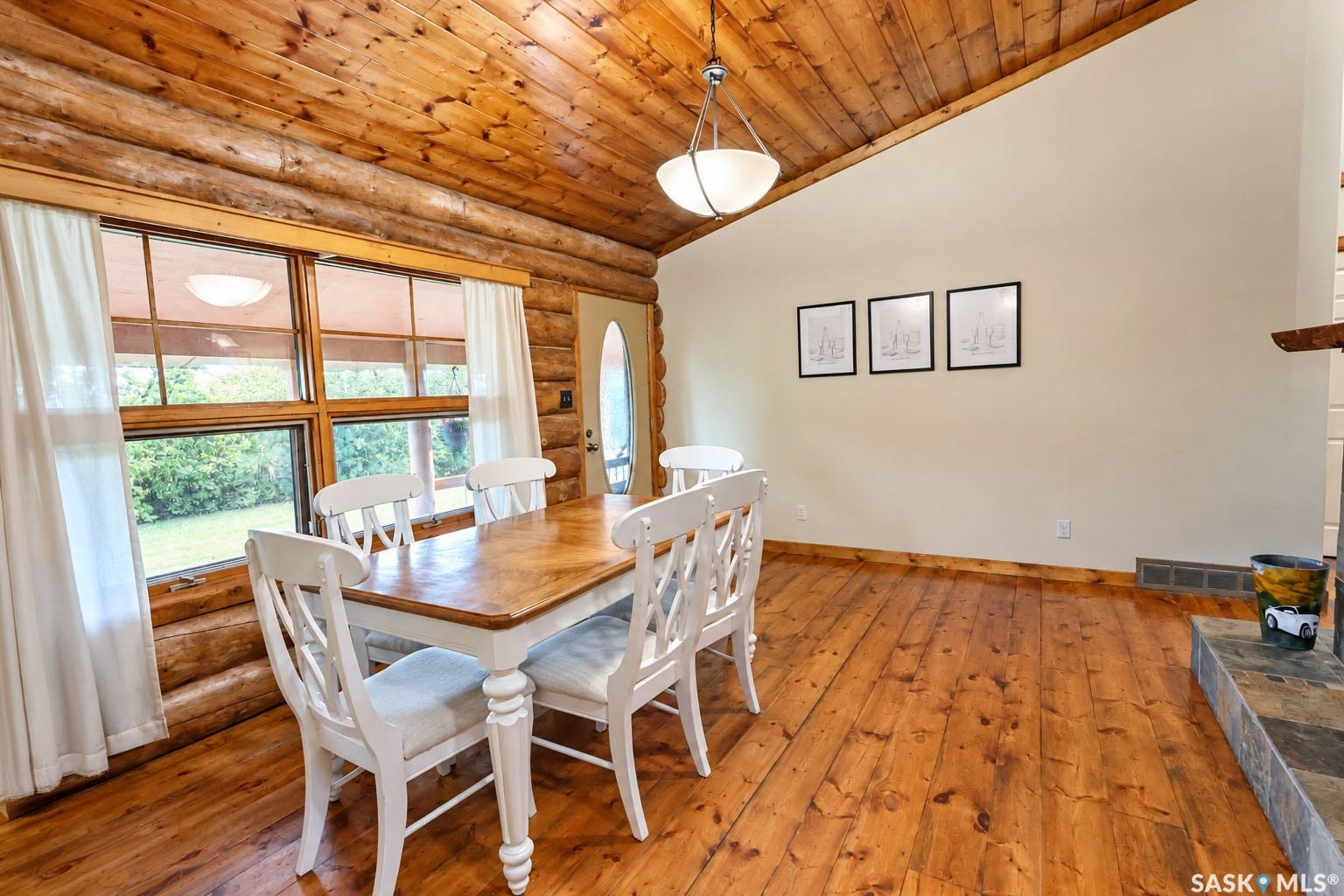 Vaulted wood-paneled ceiling, wood-finish flooring, log wall construction, multi-pane windows, and a built-in stone-finish fireplace base