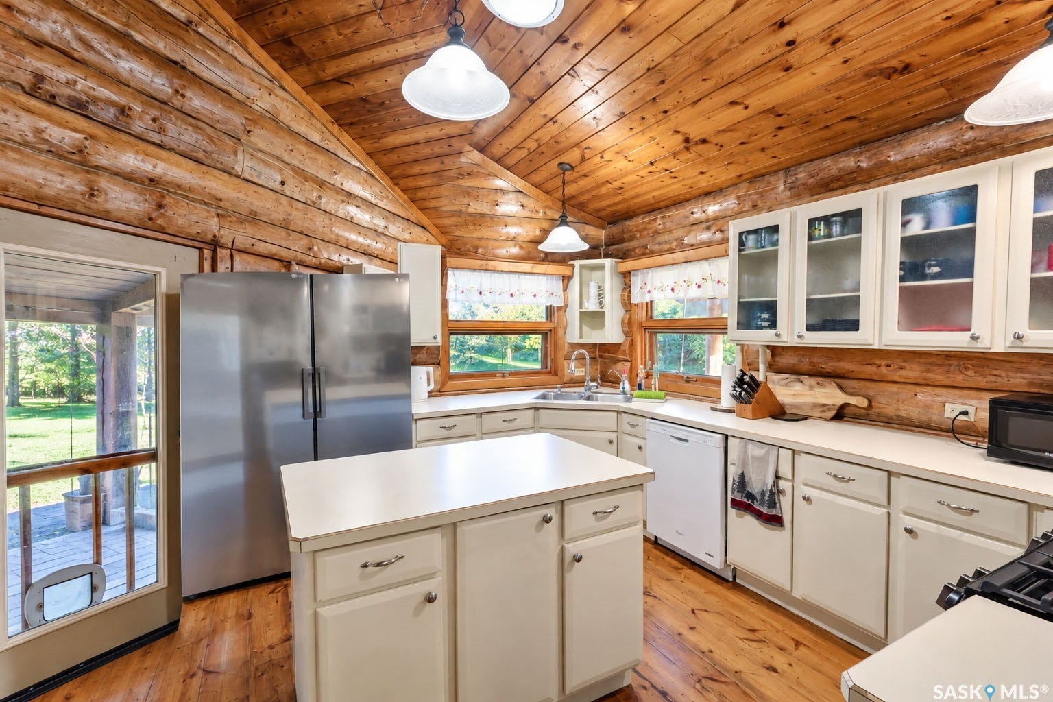 Vaulted wood-paneled ceiling, wood-finish flooring, stainless steel refrigerator, white cabinetry, and a kitchen island