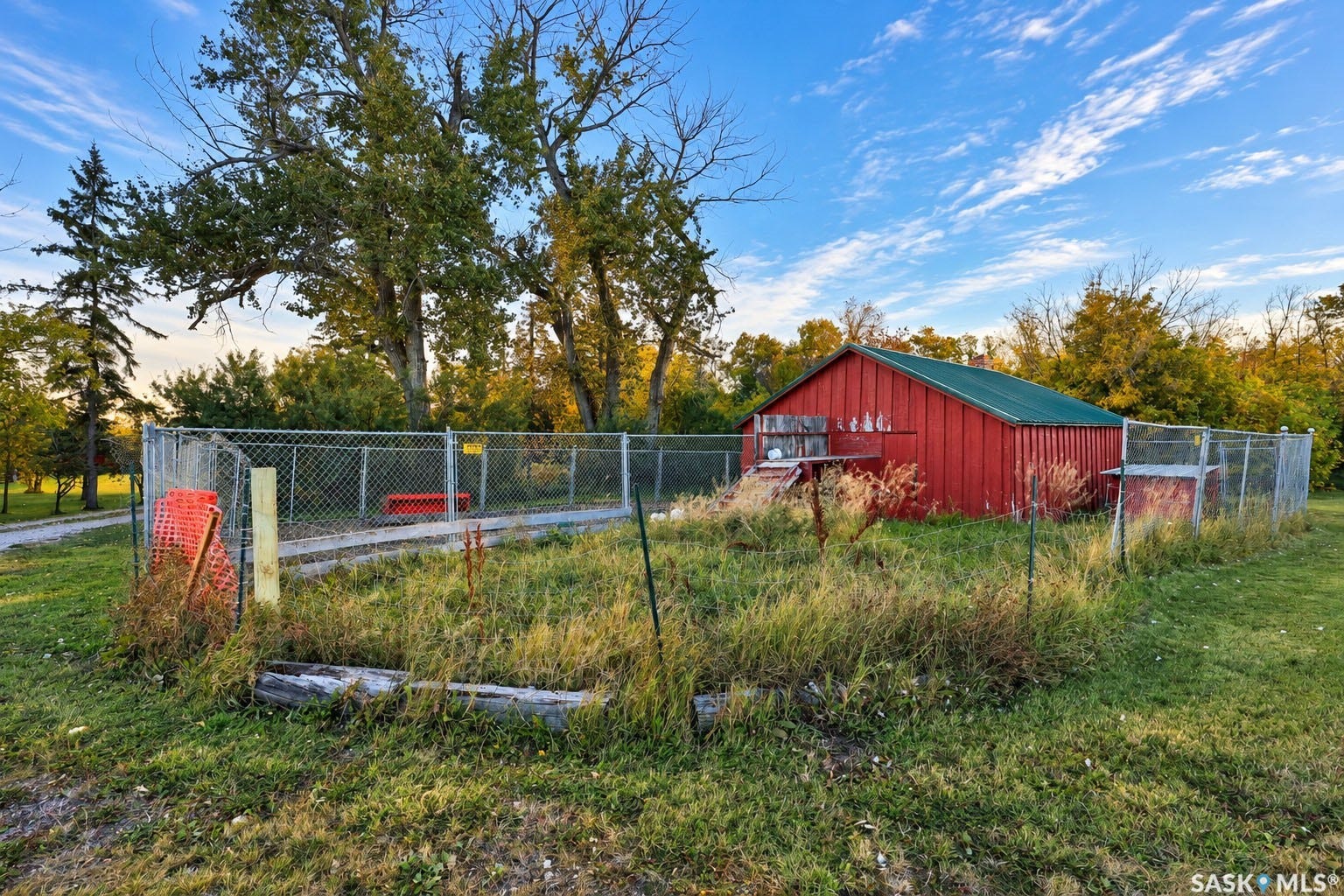 Red-sided outbuilding with a green roof, enclosed by chain-link fencing