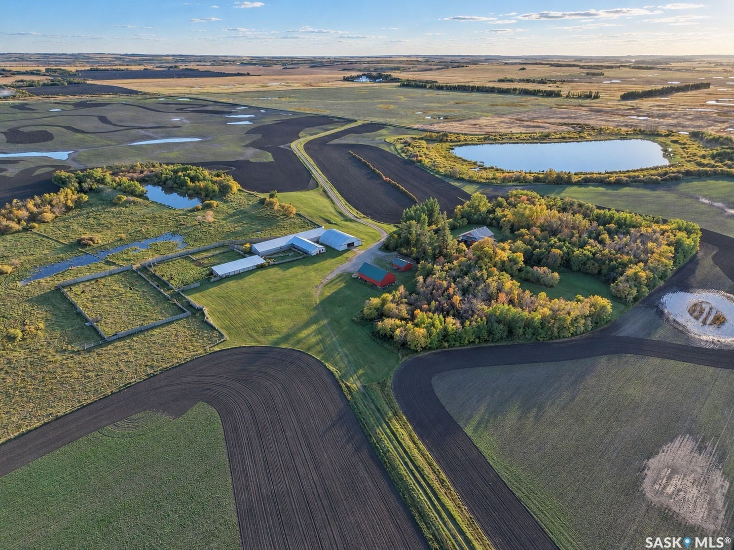 Expansive agricultural property featuring multiple outbuildings, cultivated land, a wooded area, and natural ponds