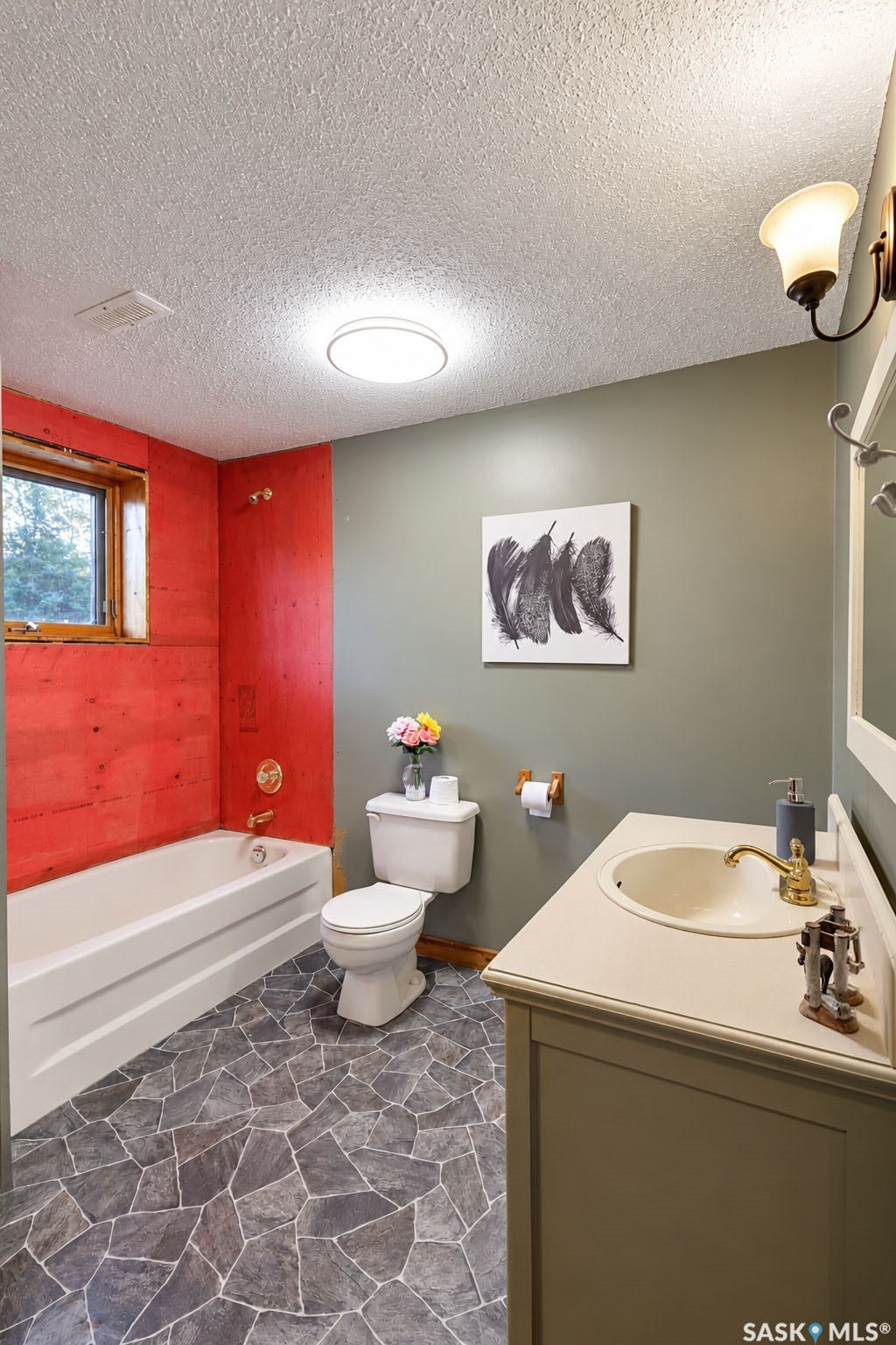 Bathroom featuring a single vanity with an integrated sink, a built-in bathtub with a gold-finish faucet, and unique geometric tile flooring