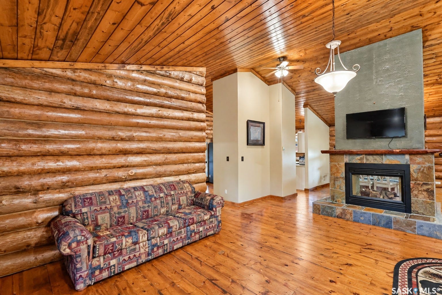 Wood-paneled ceilings, log wall construction, wood-finish flooring, and a stone-clad fireplace with a hearth