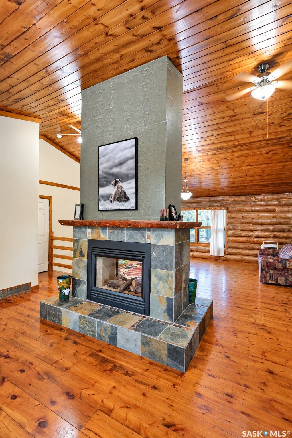 Central stone-clad fireplace with a raised hearth, wood-finish flooring, and a wood-paneled vaulted ceiling