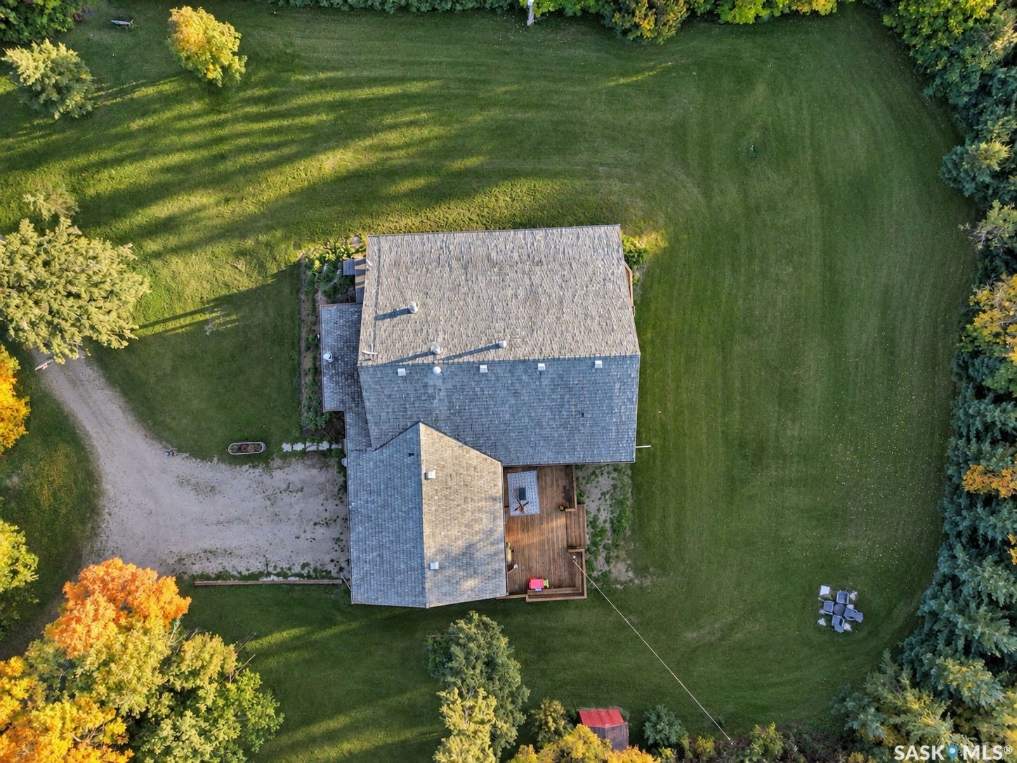 Expansive green landscape with a gravel driveway, multi-level shingle roof, and a wood deck