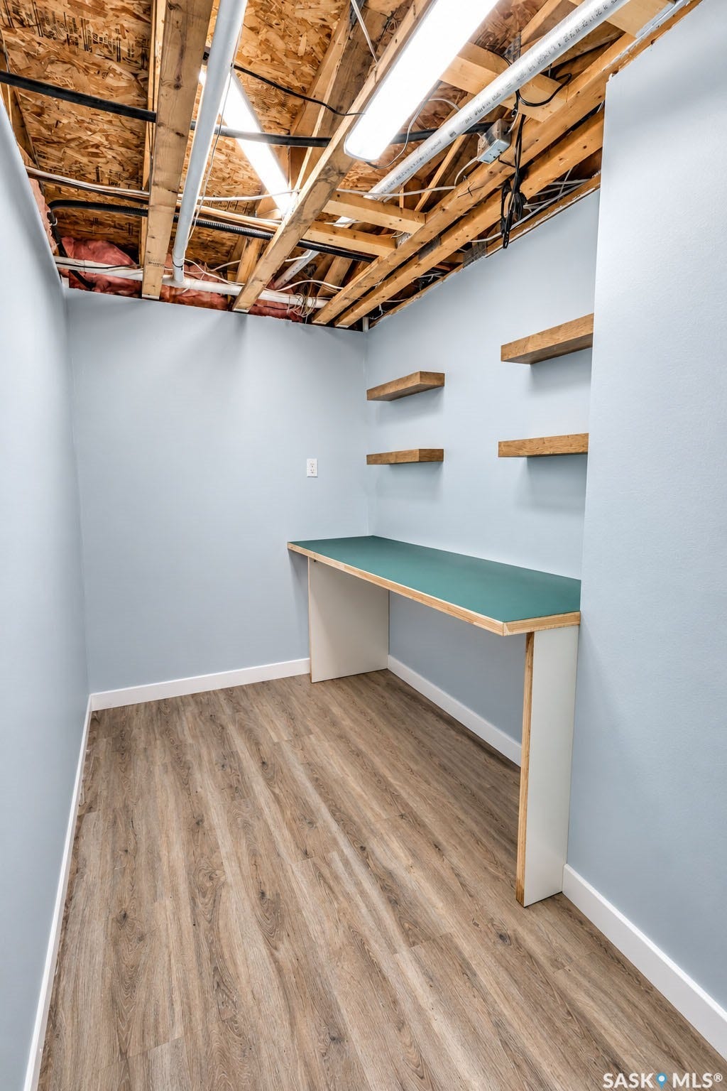 Built-in desk with a green countertop, four floating wood shelves, recessed lighting, and wood-finish flooring