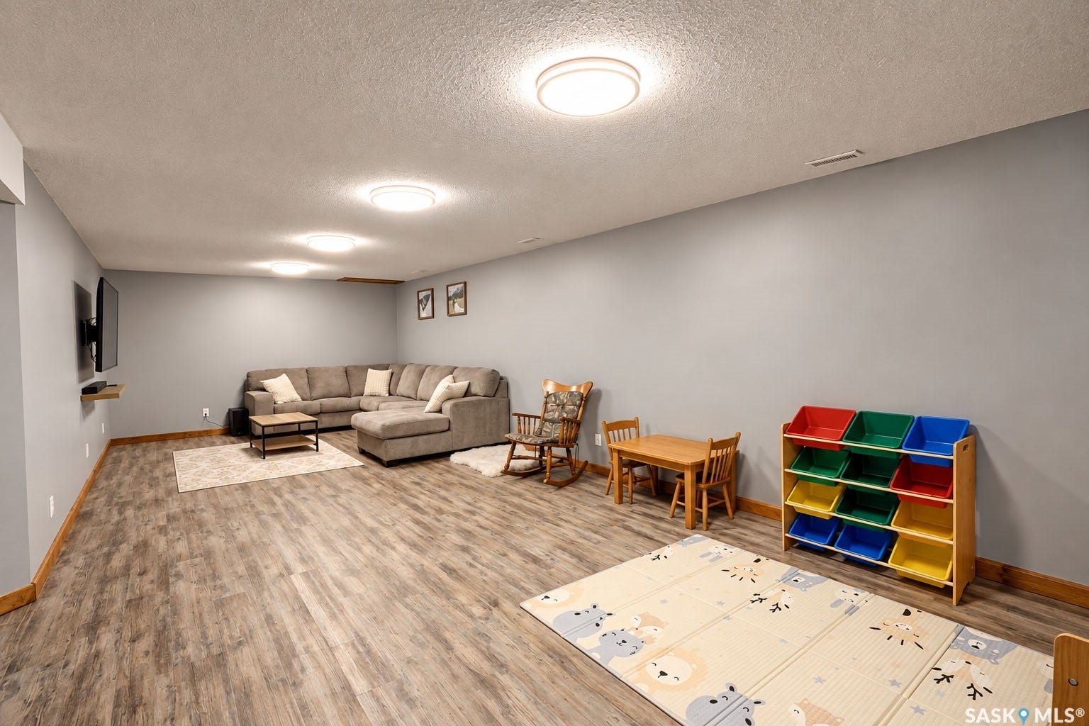 Spacious room featuring wood-finish flooring, light gray walls, and multiple ceiling-mounted flush light fixtures