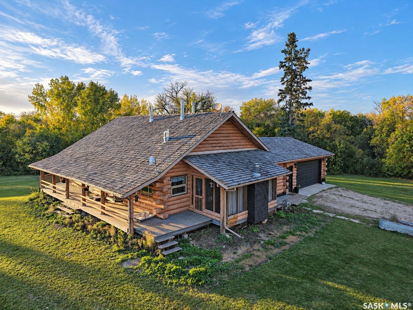 Log-style exterior with an attached two-car garage, expansive covered porch, and mature trees in the surrounding landscape