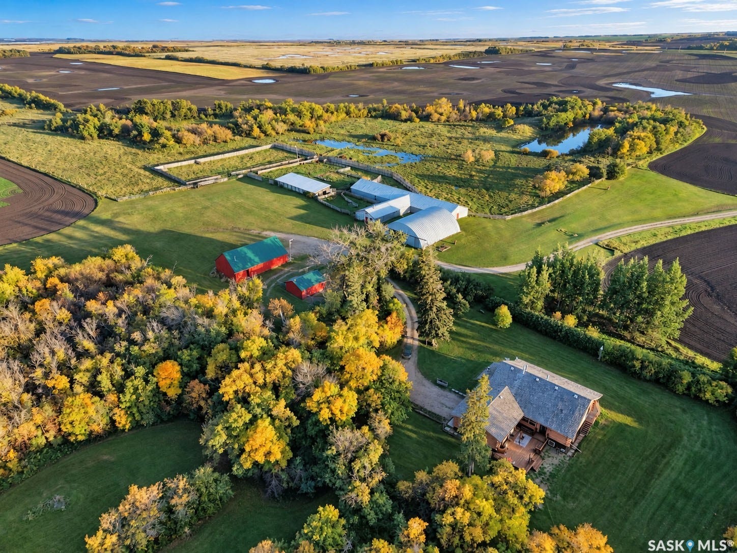 Wood-sided residence with multiple outbuildings, agricultural land, and surrounding wooded areas