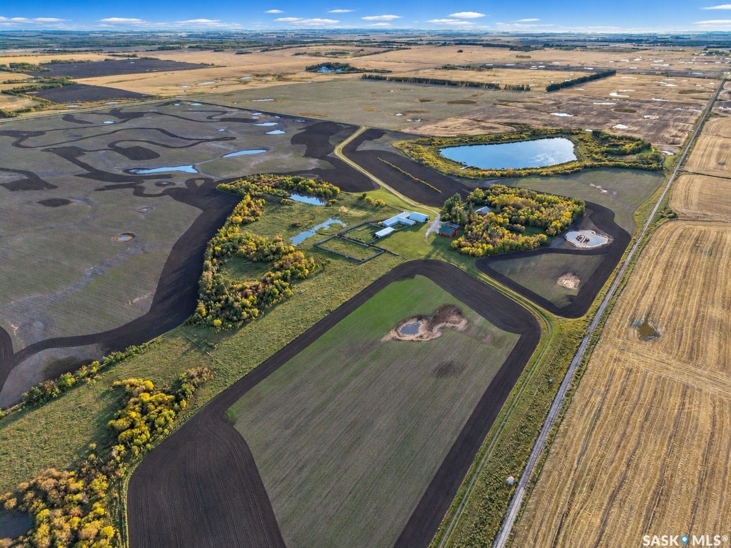 Expansive land with multiple cultivated fields, a substantial pond, a central cluster of buildings, and a network of unpaved roads