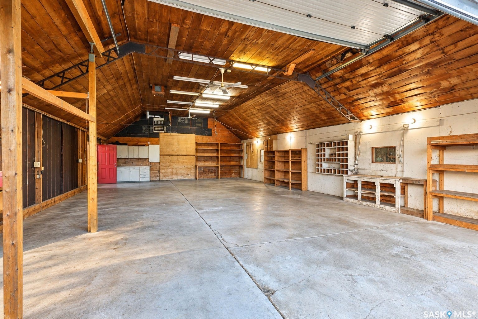 Spacious garage featuring a concrete floor, wood-paneled vaulted ceiling, extensive built-in shelving, and integrated overhead lighting