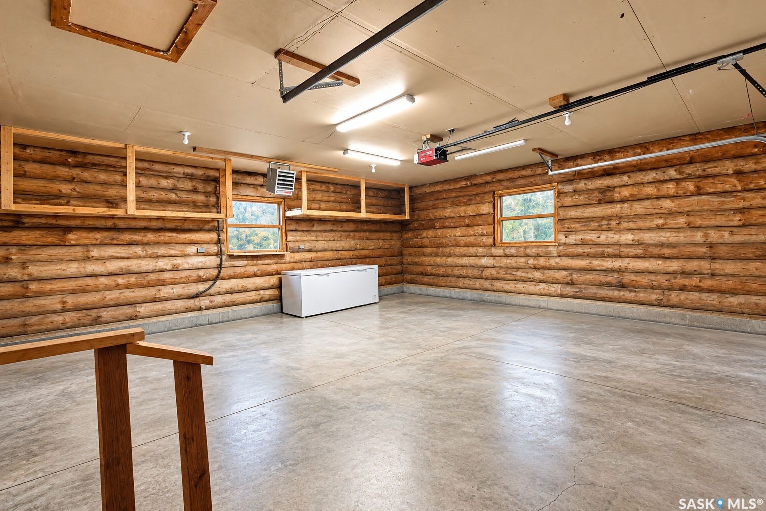 Concrete flooring, wood-paneled walls, built-in wooden shelving, two windows with natural light, and overhead fluorescent lighting