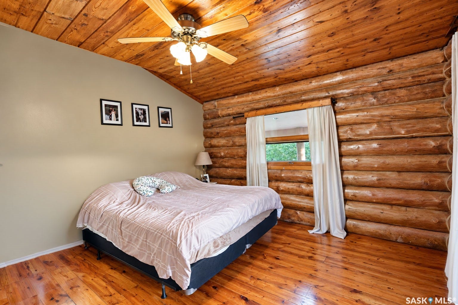Vaulted wood-paneled ceiling with ceiling fan, log wall construction, wood-finish flooring, and a window with drapes