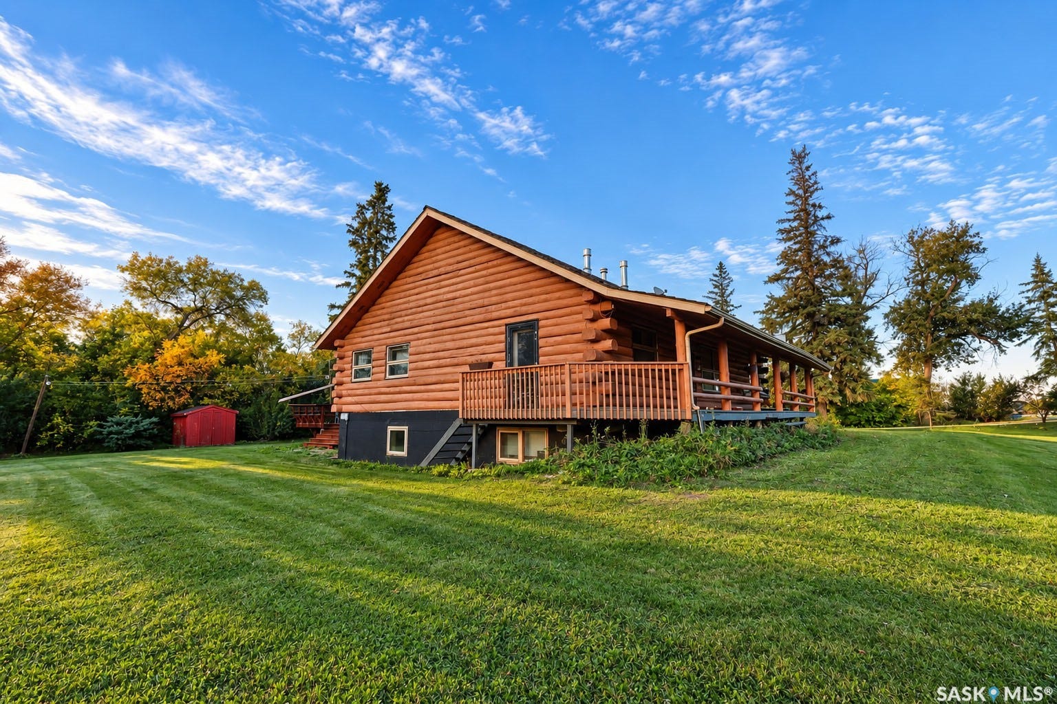 Log-style exterior with a covered porch, wood railing, and a sloped lawn