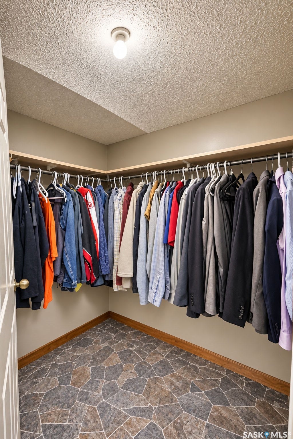 Walk-in closet featuring extensive built-in shelving and hanging rods, overhead lighting, and stone-look flooring