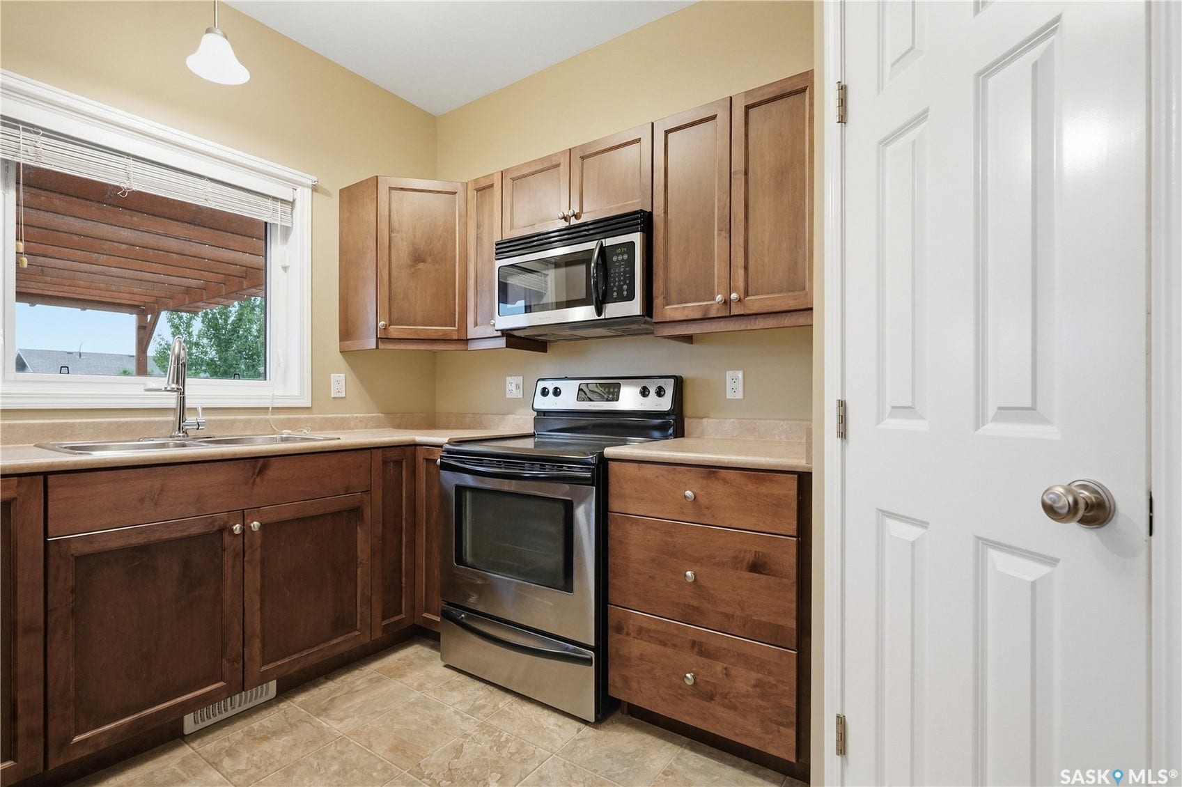 Kitchen featuring wood-finish cabinetry, stainless steel appliances, a corner sink with a window, and tile flooring