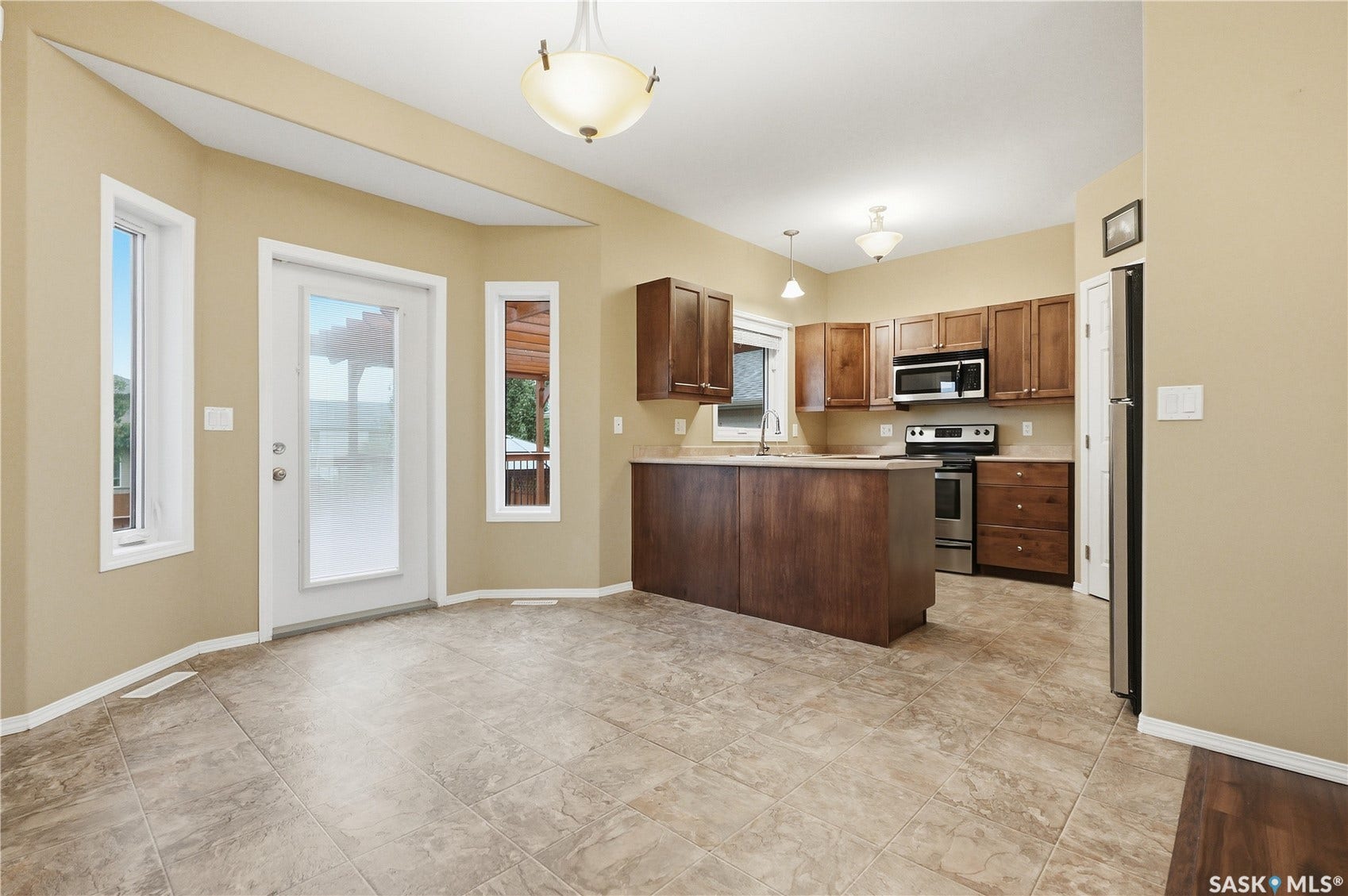 Kitchen and dining area featuring ceramic tile flooring, wood cabinetry, stainless steel appliances, and a central island