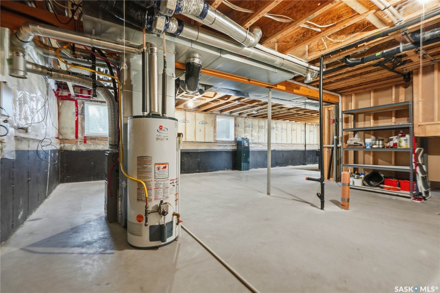 Unfinished basement space with concrete flooring, exposed ceiling joists, and a water heater