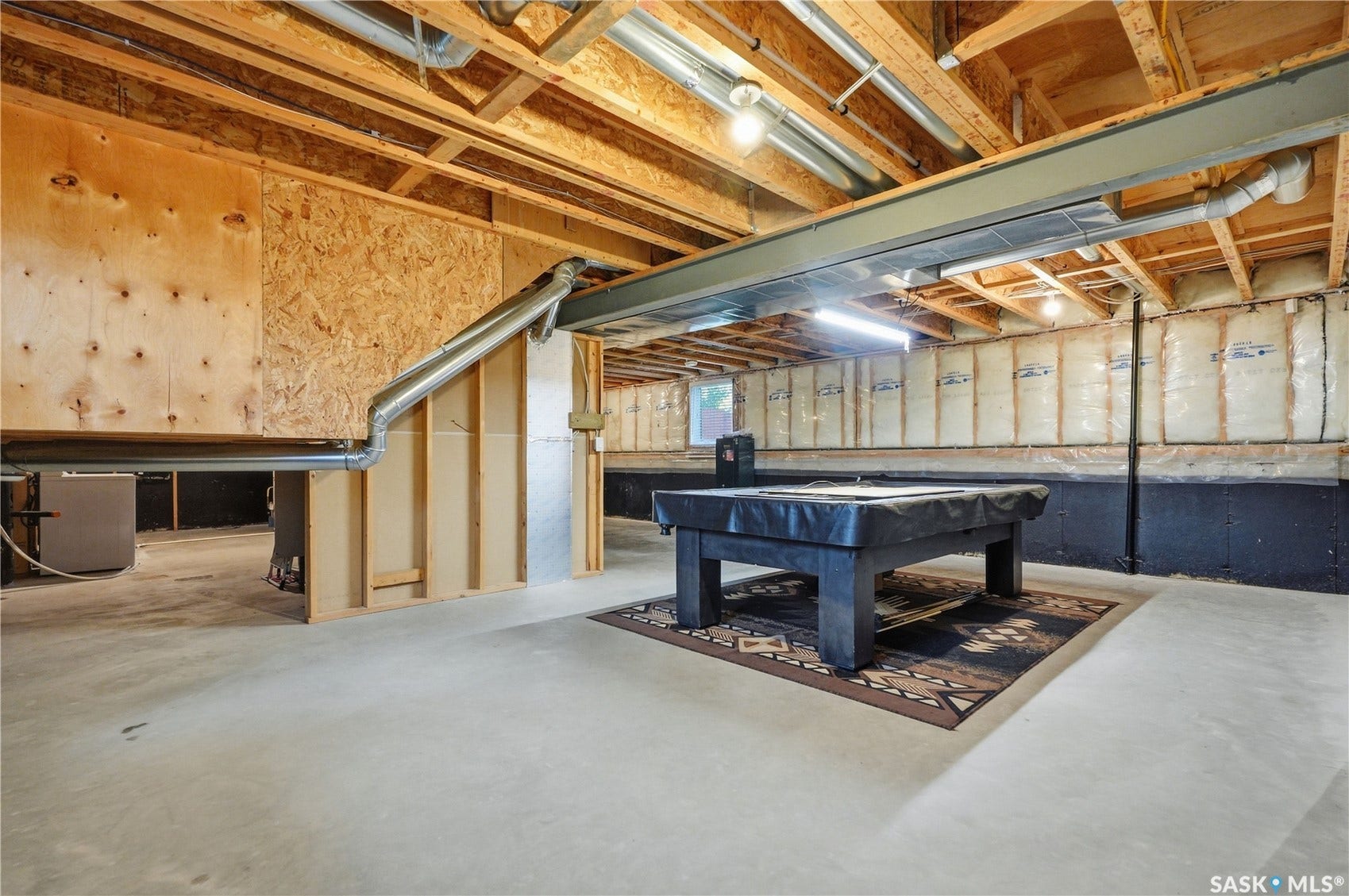 Unfinished basement featuring exposed wood joists, concrete flooring, and insulated perimeter walls