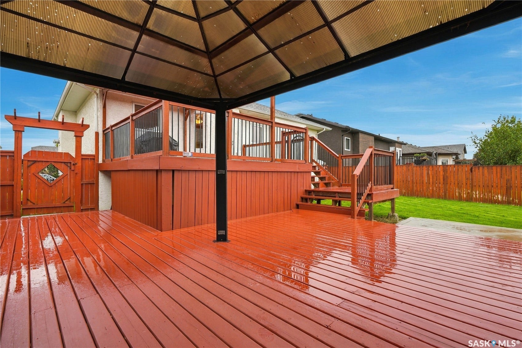 Expansive wooden deck with a covered gazebo, staircase access, fenced perimeter, and grass area