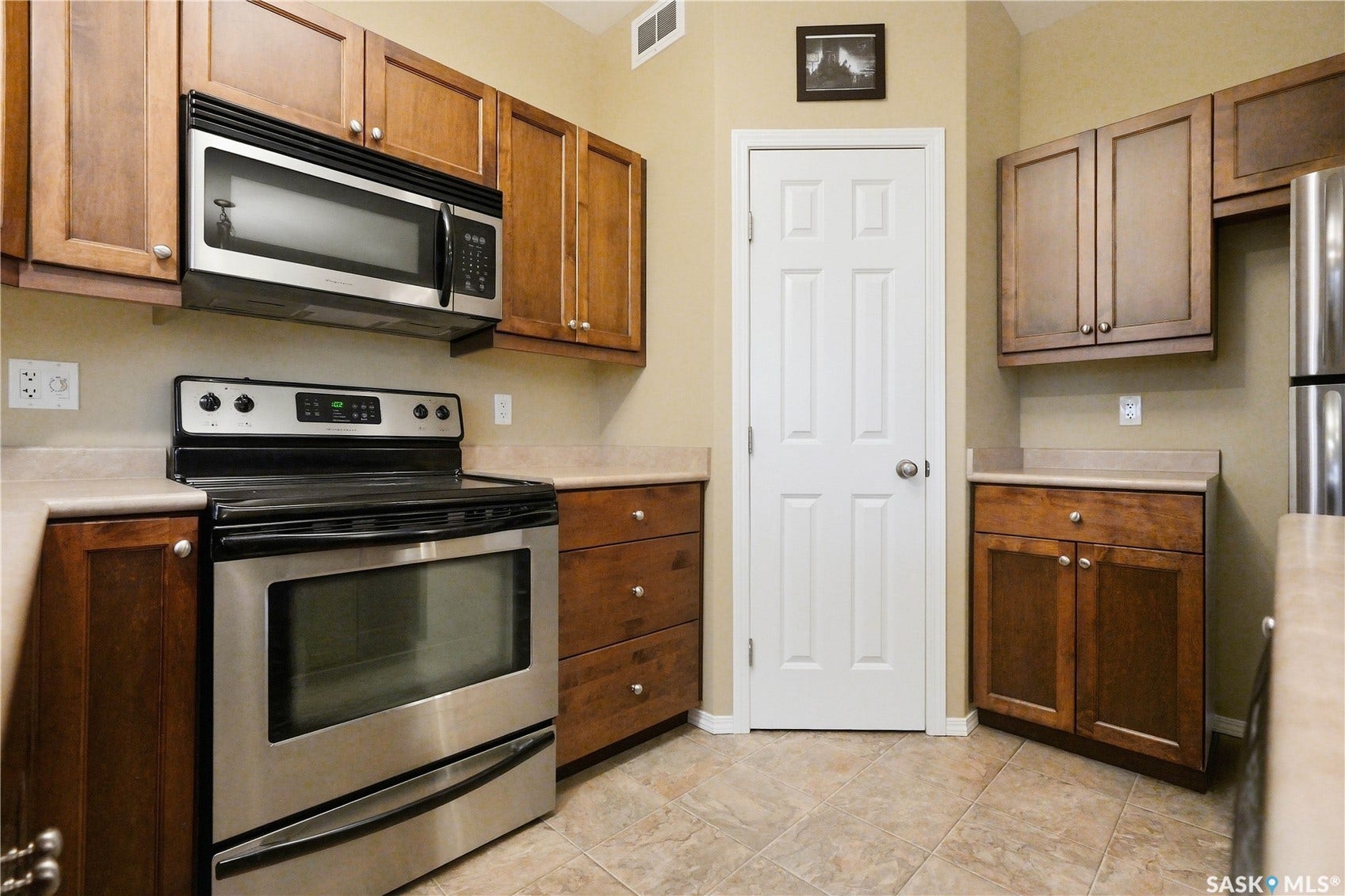 Kitchen featuring wood cabinetry, stainless steel appliances, neutral countertops, and tile flooring
