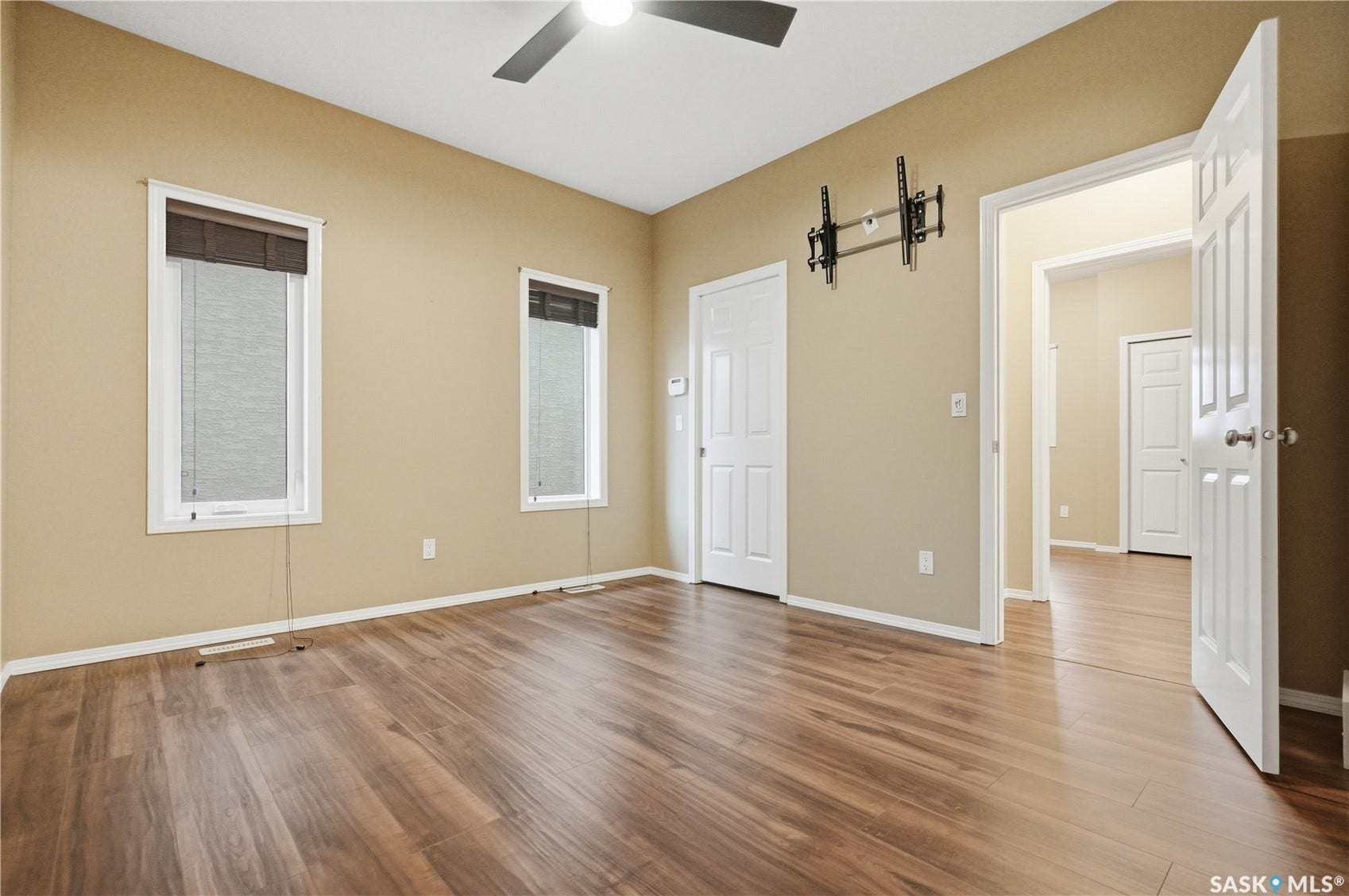 Wood-finish flooring, two large windows, white paneled doors, and a ceiling fan