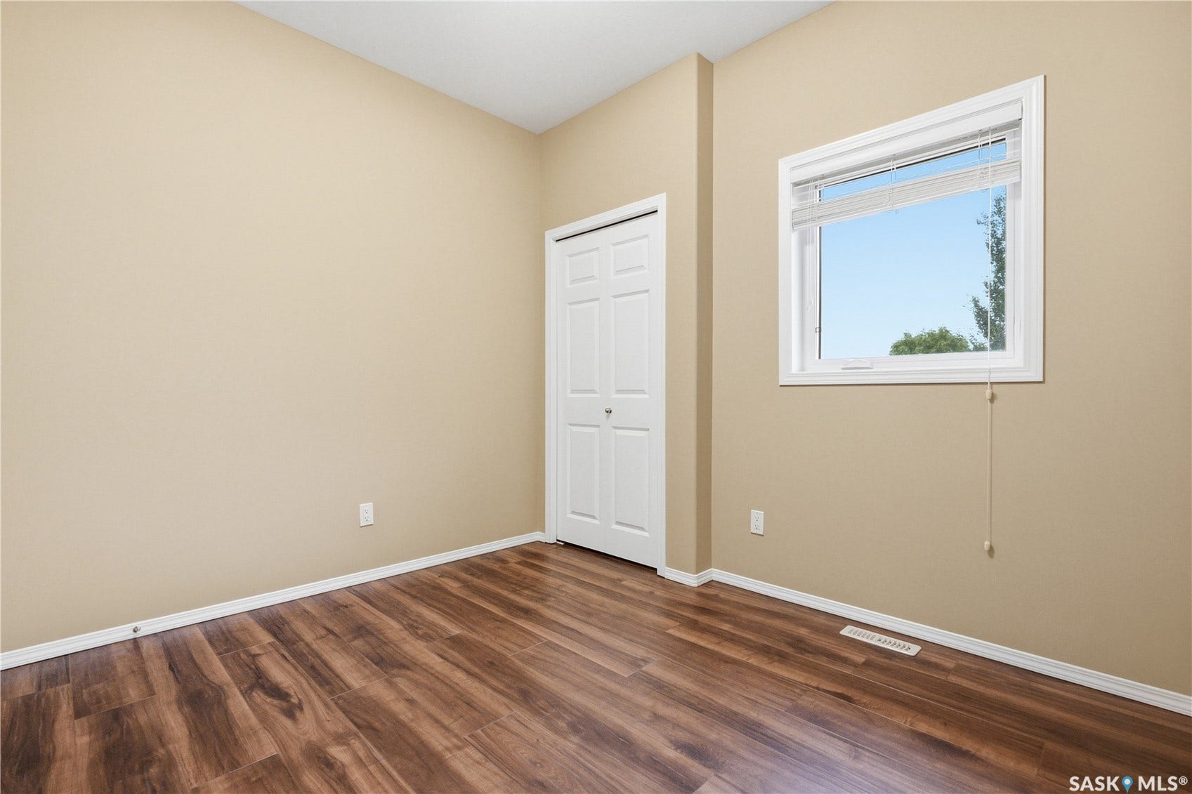 Wood-finish flooring, white trim, bi-fold closet doors, and window with blinds