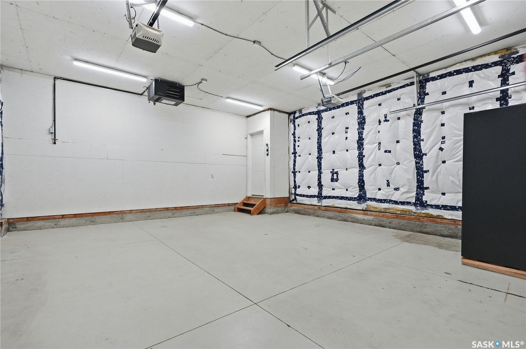 Concrete flooring with exposed ceiling joists, linear fluorescent lighting, built-in wall insulation, and a wooden stair entry