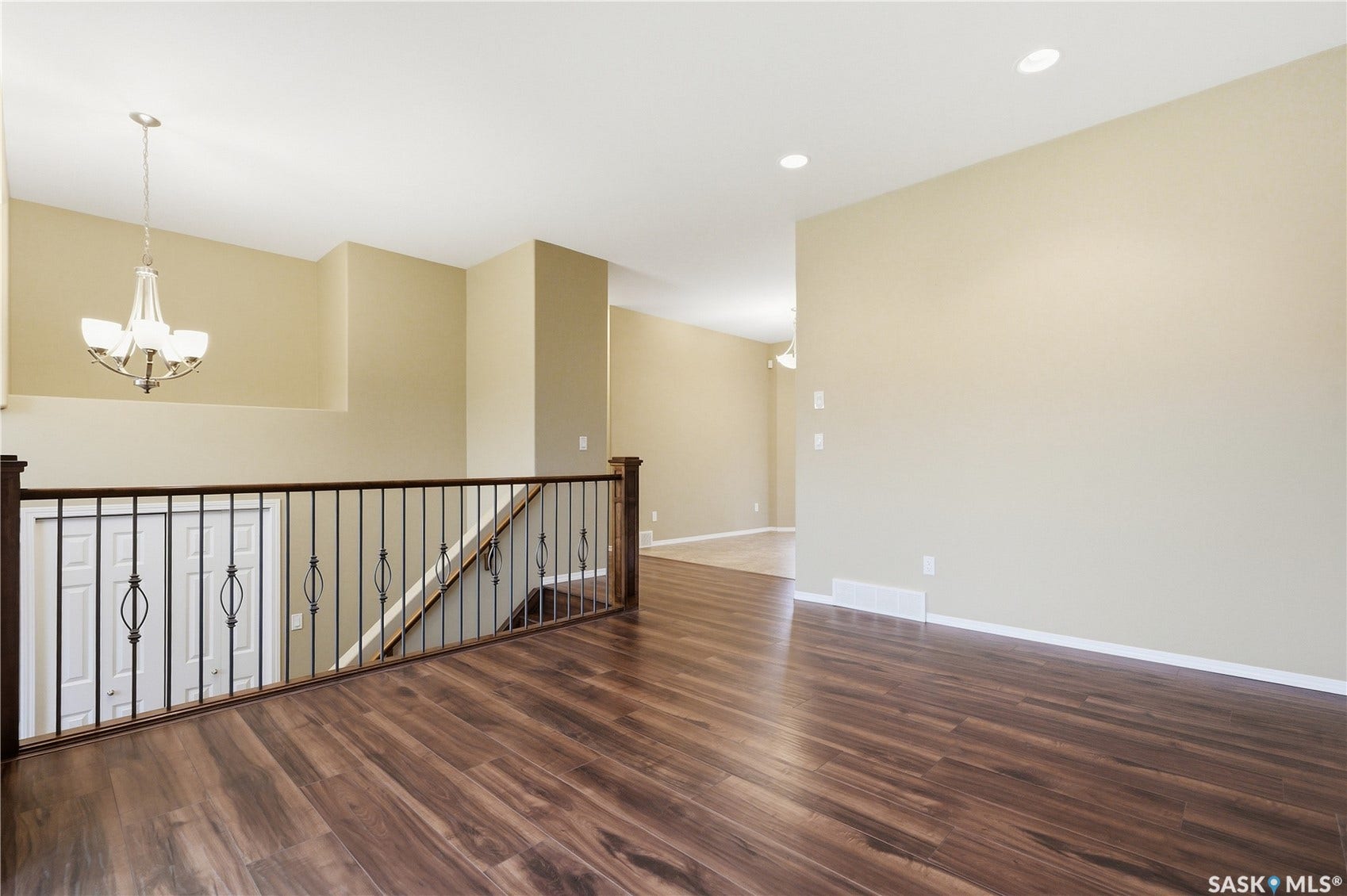 Wood-finish flooring, recessed lighting, chandelier, and a dark wood and wrought iron railing