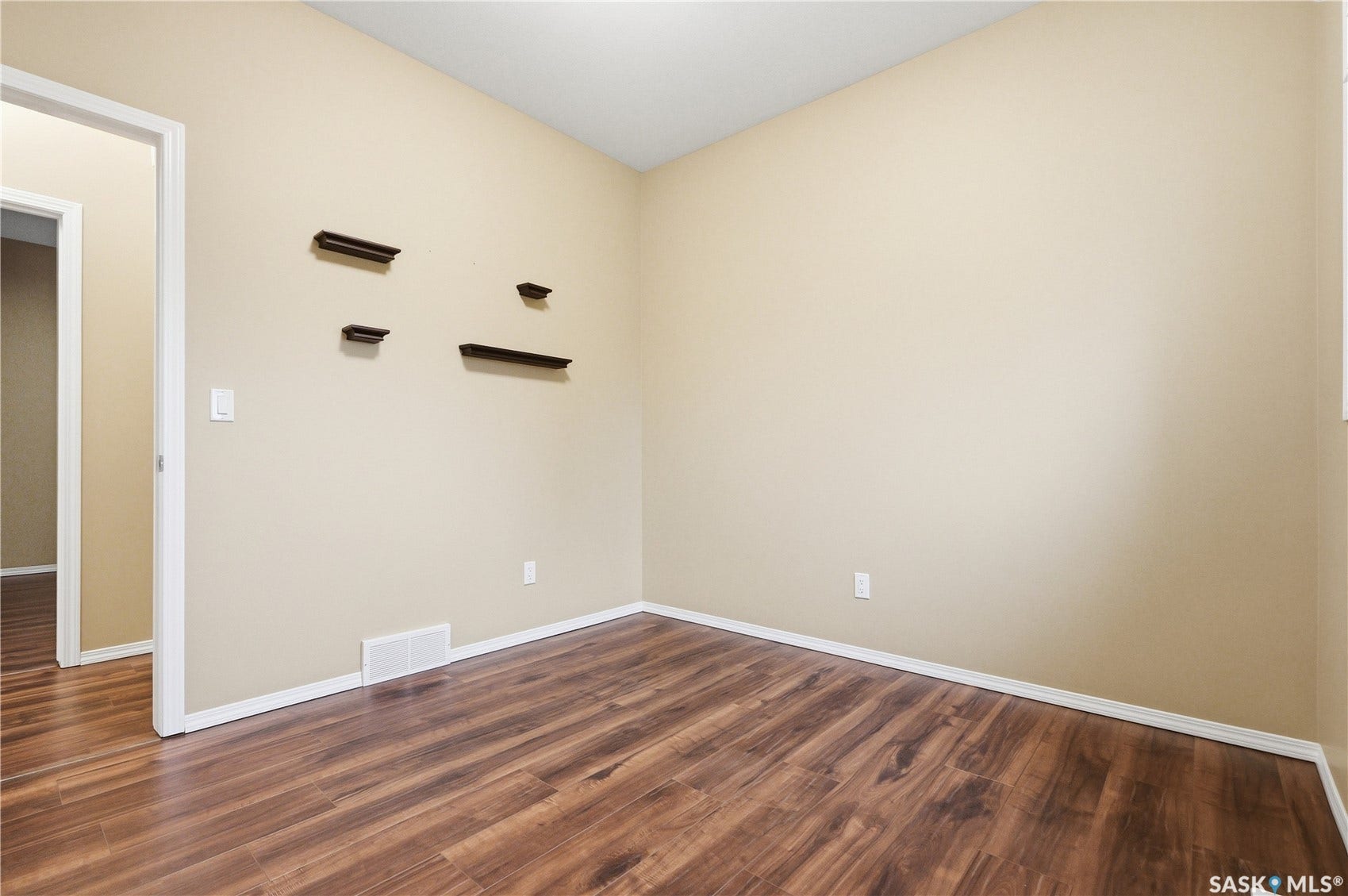 Wood-finish flooring with white trim, neutral wall color, and built-in wall shelves