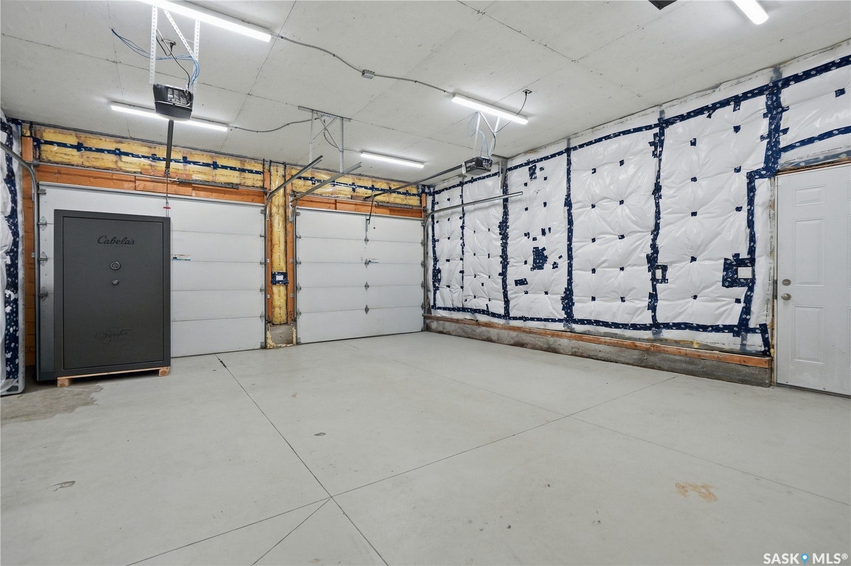 Concrete flooring, two overhead garage doors, exposed wood framing, white insulation on wall, and a white access door