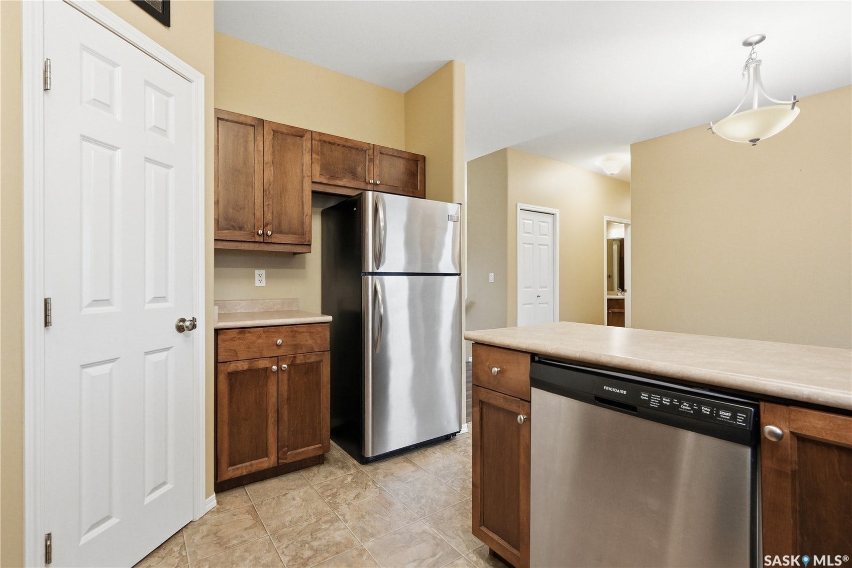 Stainless steel refrigerator, wood-finish cabinetry, tile flooring, and a stainless steel dishwasher