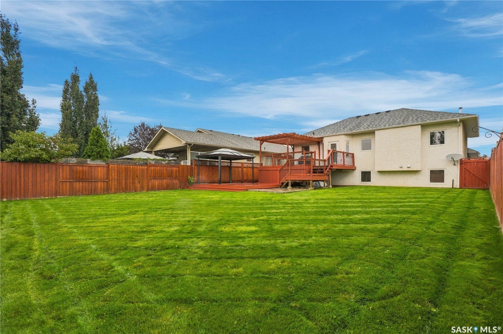 Expansive lawn area with a wood privacy fence, multi-level wood deck, and a wood pergola